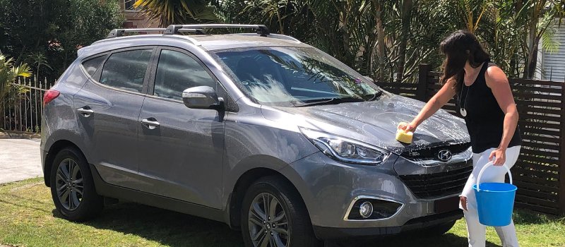 A woman washing her car with a sponge and bucket