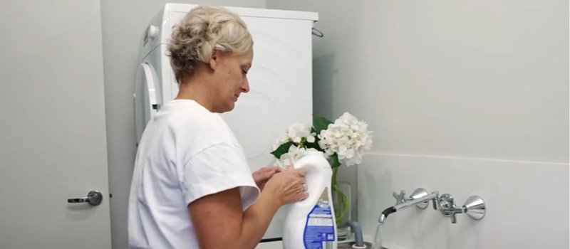 Woman putting washing liquid into washing machine