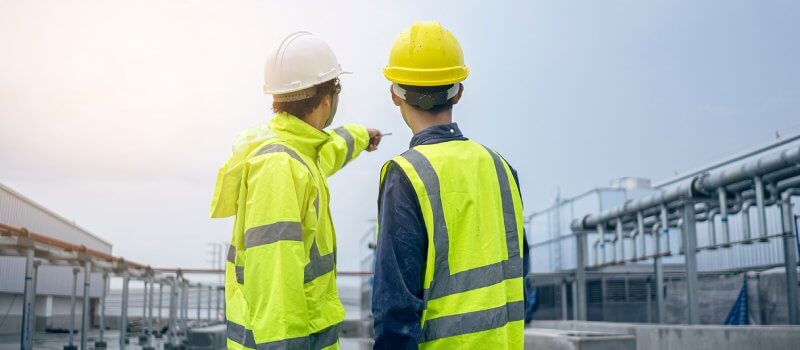 Two people in high vis clothing pointing at a pipes on a construction site