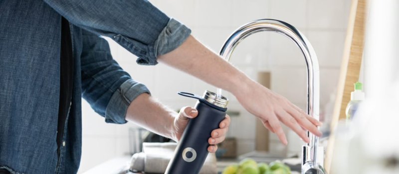 A person filling up a black water bottle at the kitchen sink 