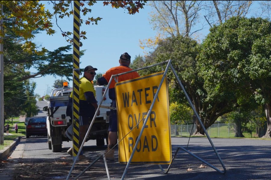 Water over road sign with men in hi vis standing in background