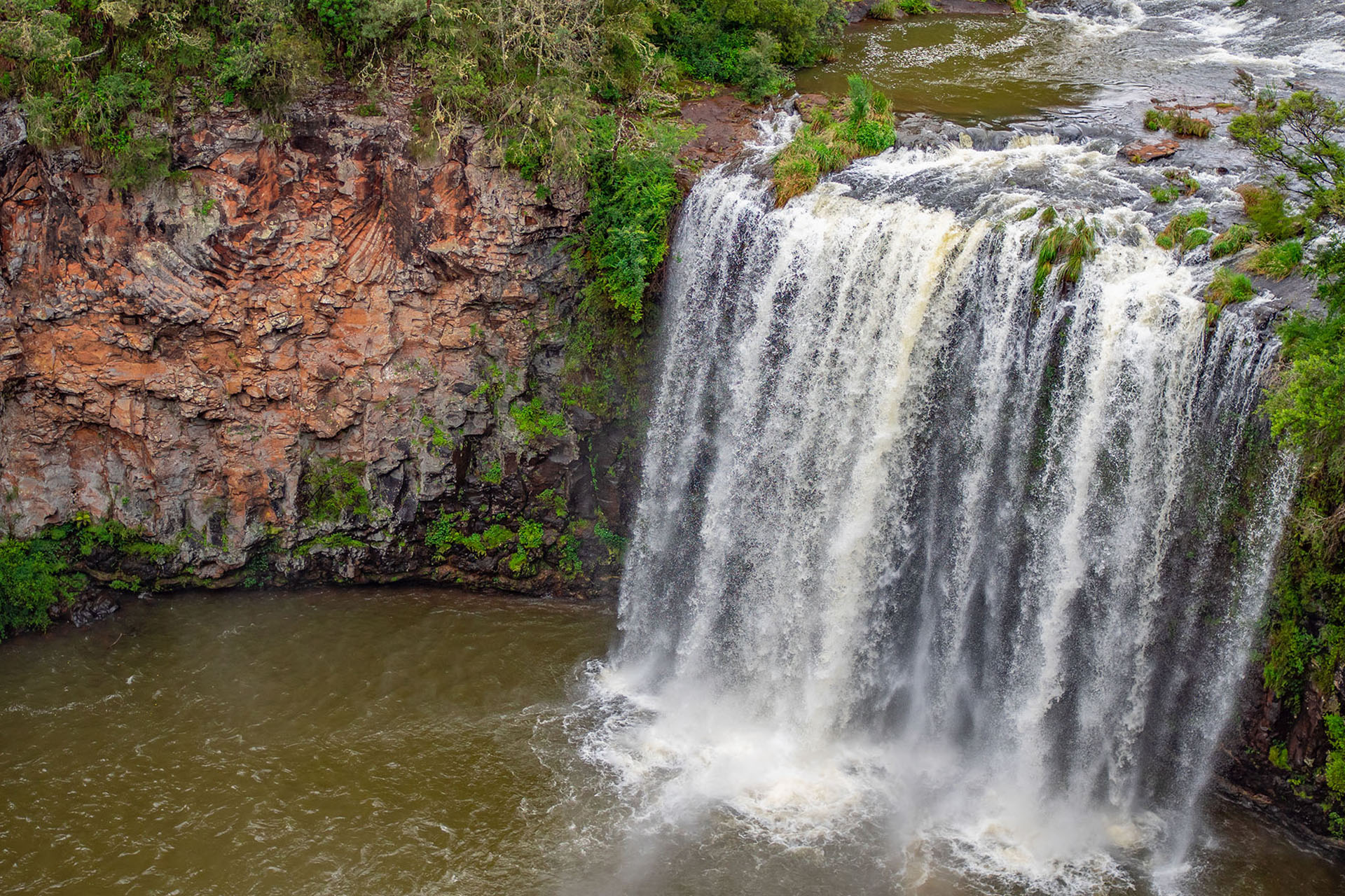 A high angle photo of a tall waterfall washing over rocky terrain