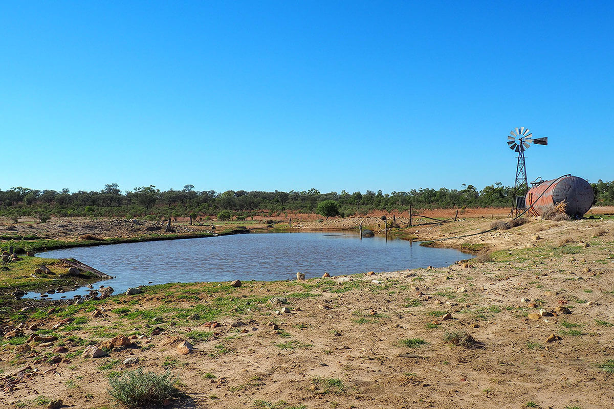 a small dam with a windmill and tank to the right