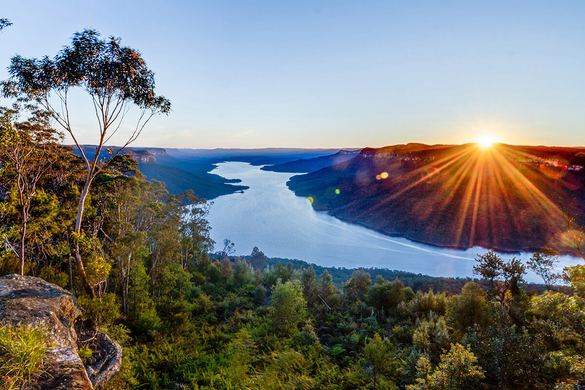 a view down from a cliff towards a lake. There are lots of gum trees and the sun is setting