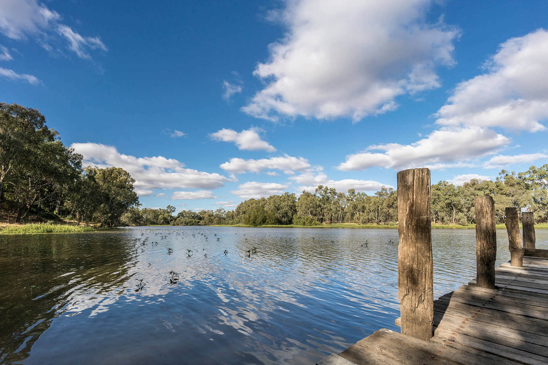 a river with ripples and a wooden pier with small pylons