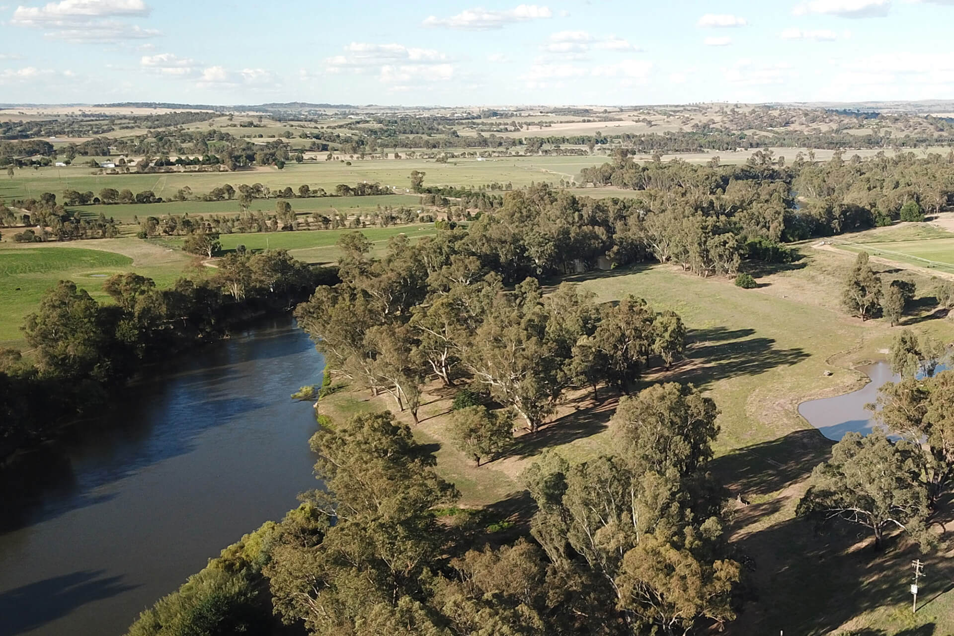 A river surrounded by open green fields. There are trees along the banks of the river