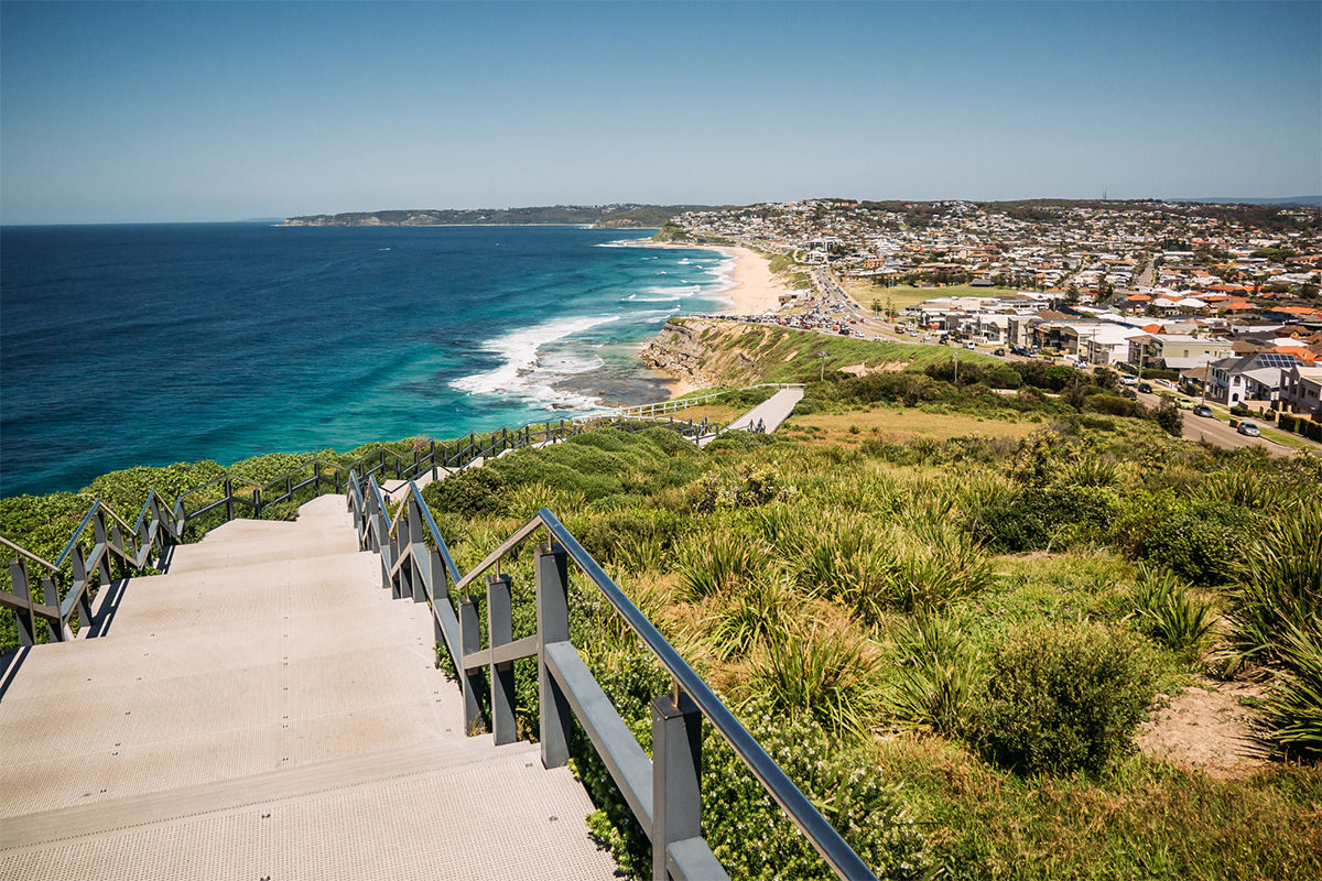 a set of stairs leading down to a beach with houses lining the coast to the right