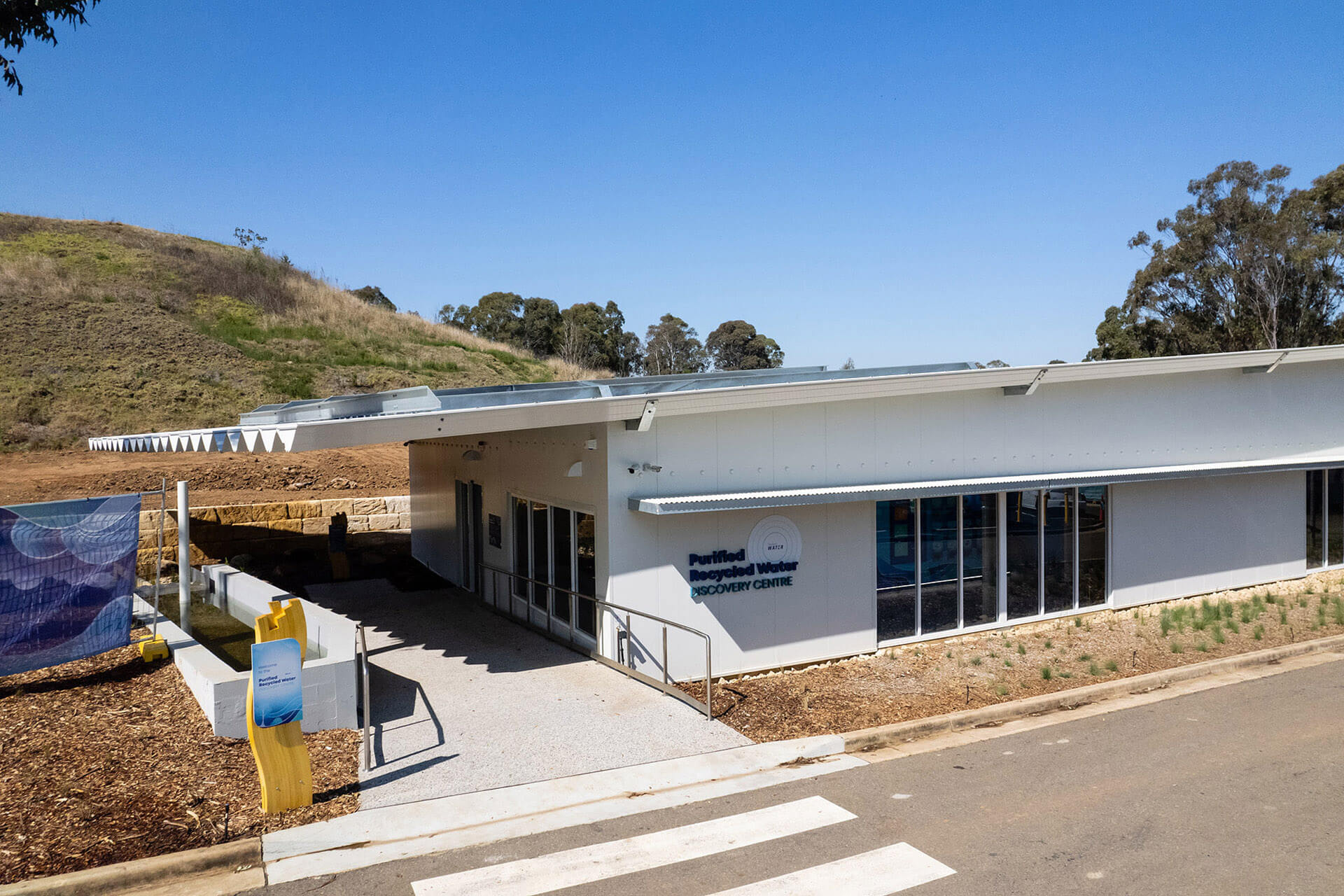 a one storey white building with an awning identified as a purified recycled water recovery centre on a sign