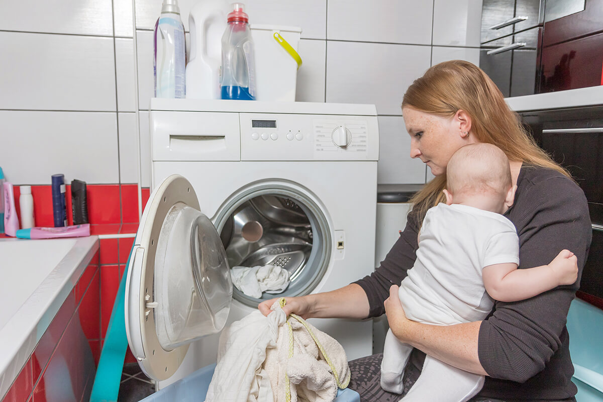 Woman holding a baby loading a washing machine 